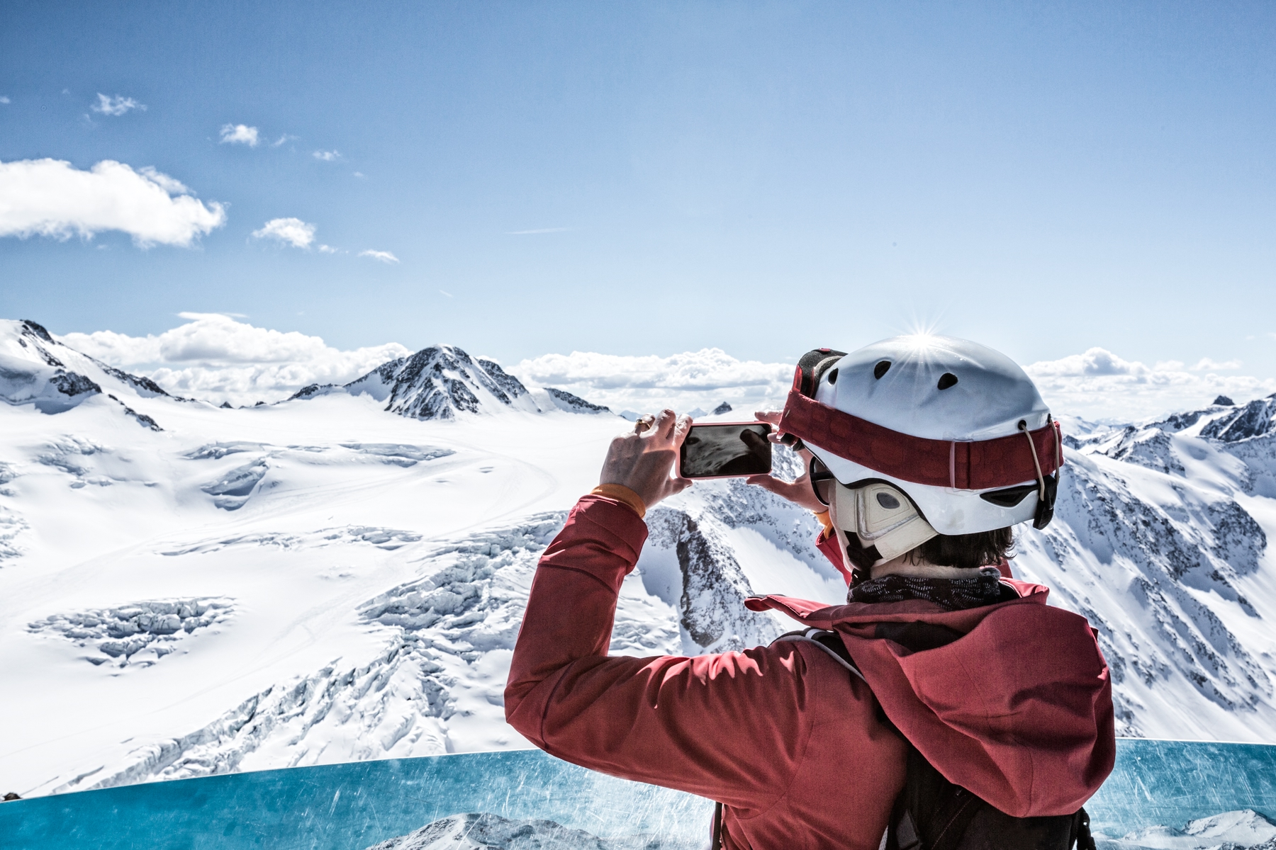 Skiier standing at top of mountain taking a photo of the scenery on their smartphone