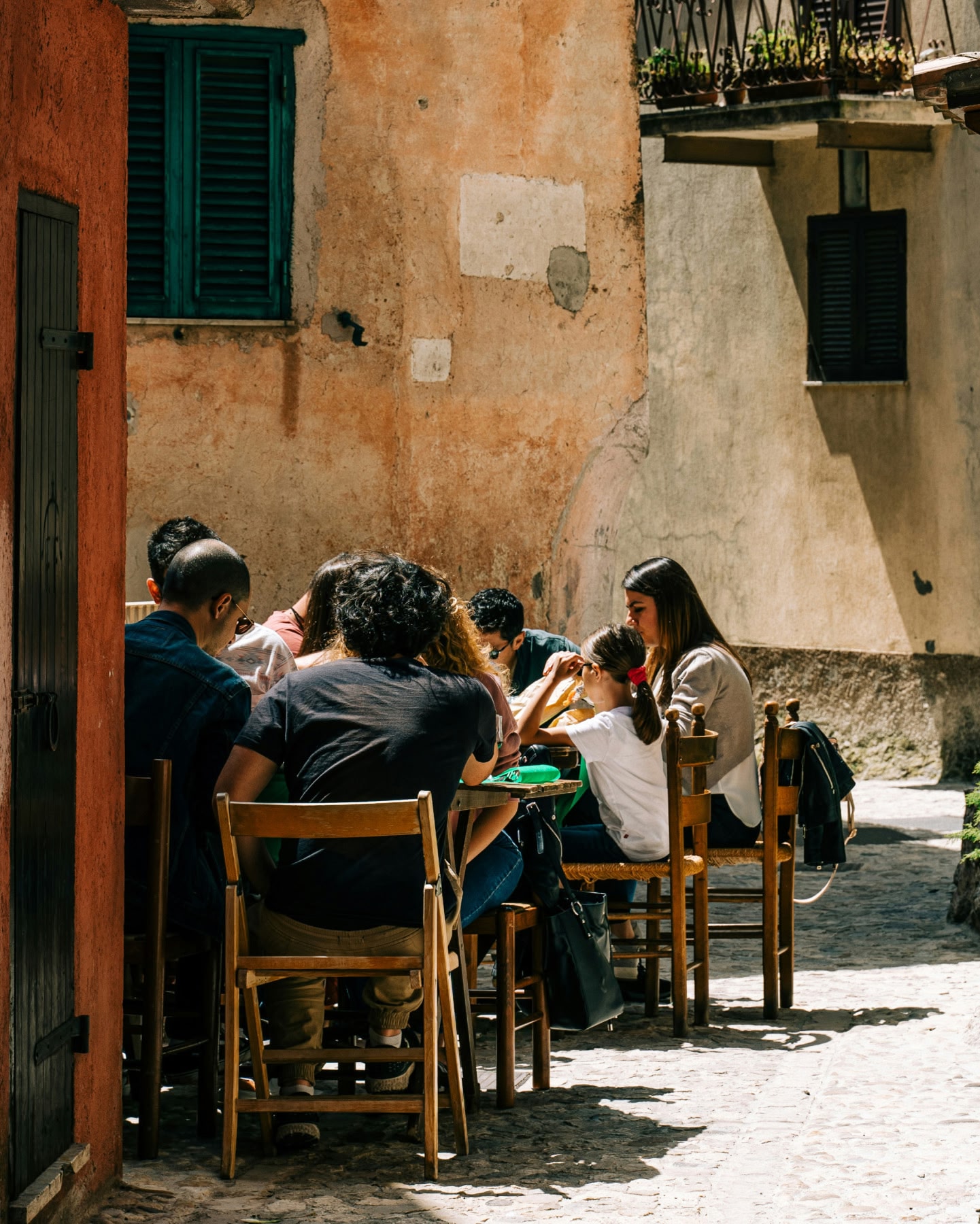 Pessoas sentadas em mesas de restaurante ao ar livre em uma pequena praça.