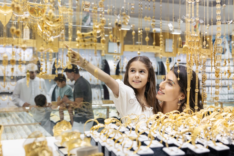 Femme tenant sa fille en l'air pour regarder les colliers suspendus au toit dans le souk de l'or.