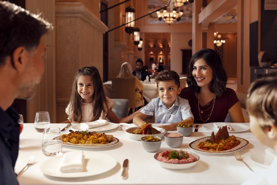 Femme et deux enfants profitant d'un festin de nourriture émiratie dans un restaurant chic.
