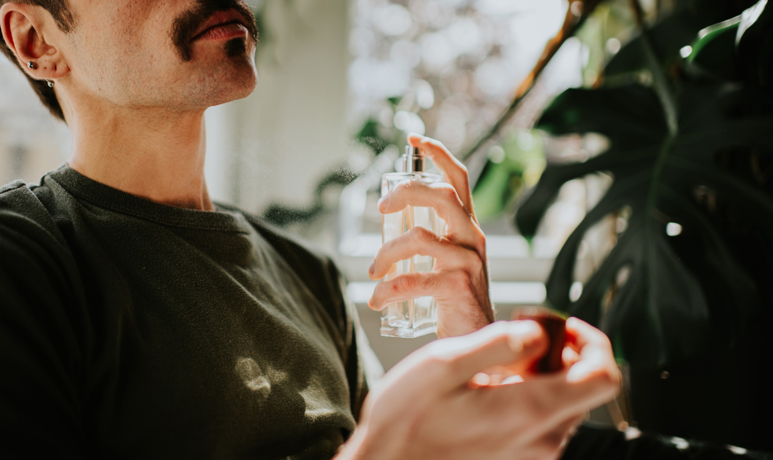 Un hombre con bigote se rocía el cuello con una fragancia de un frasco