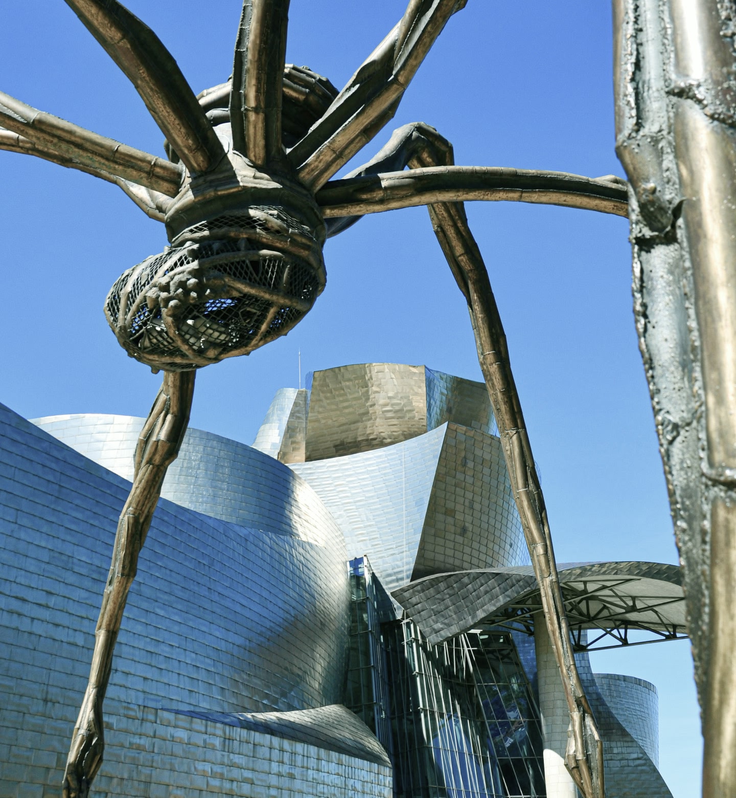 Ground-level view of the spider sculpture at the Guggenheim Museum, Bilbao, against a bright blue sky