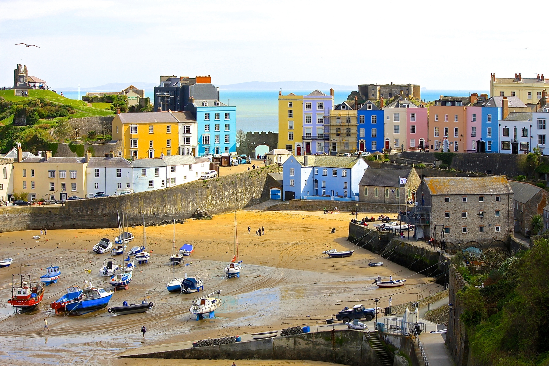 Colourful pastel houses in Tenby, a top place for spring holidays. A harbour is in the foreground with a golden beach and fishing boats.