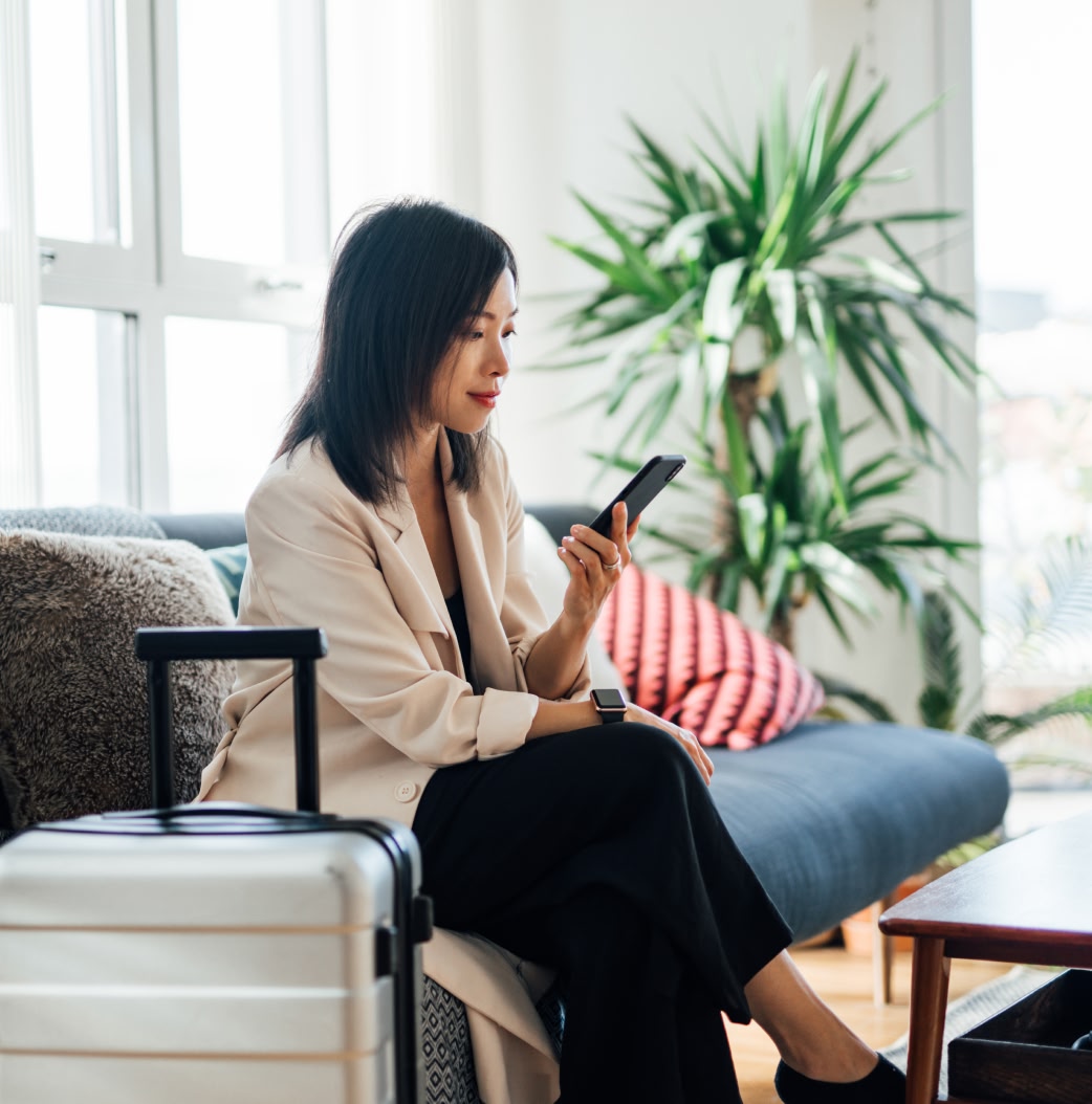 Person checking phone sitting down next to suitcase. 