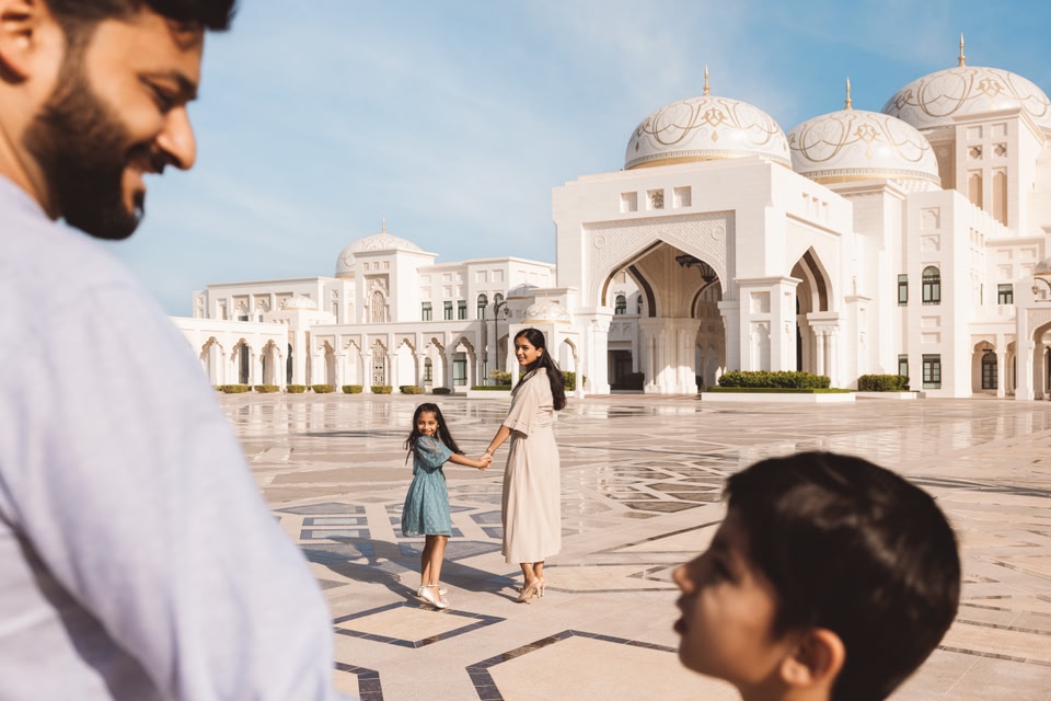 Une famille se tient devant le palais présidentiel. Le père et le fils sont au premier plan tandis que la mère et la fille attendent plus près du bâtiment.