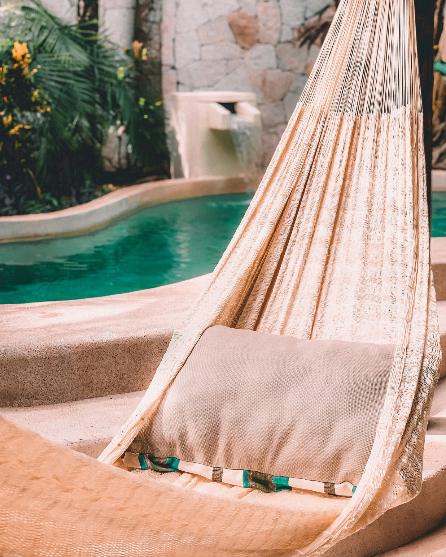 ターコイズブルーのプールの横に吊るされたクリーム色のハンモック。