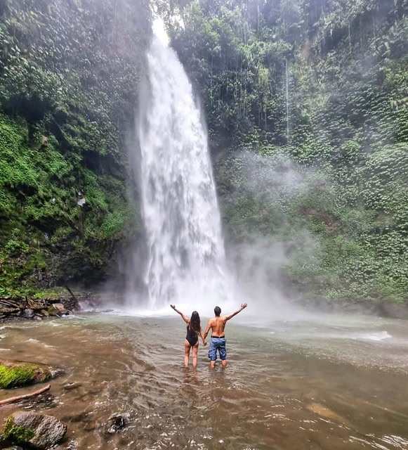 Ein Paar steht vor einem Wasserfall im Dschungel auf Bali