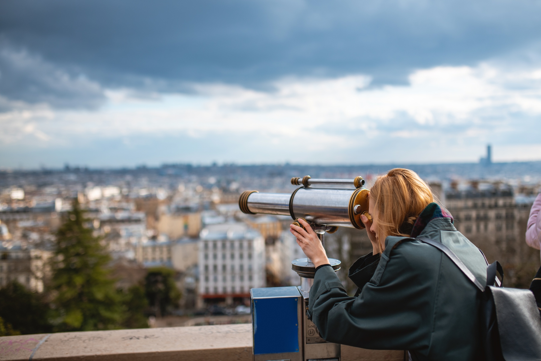 Young woman looking through a telescope at the city.
