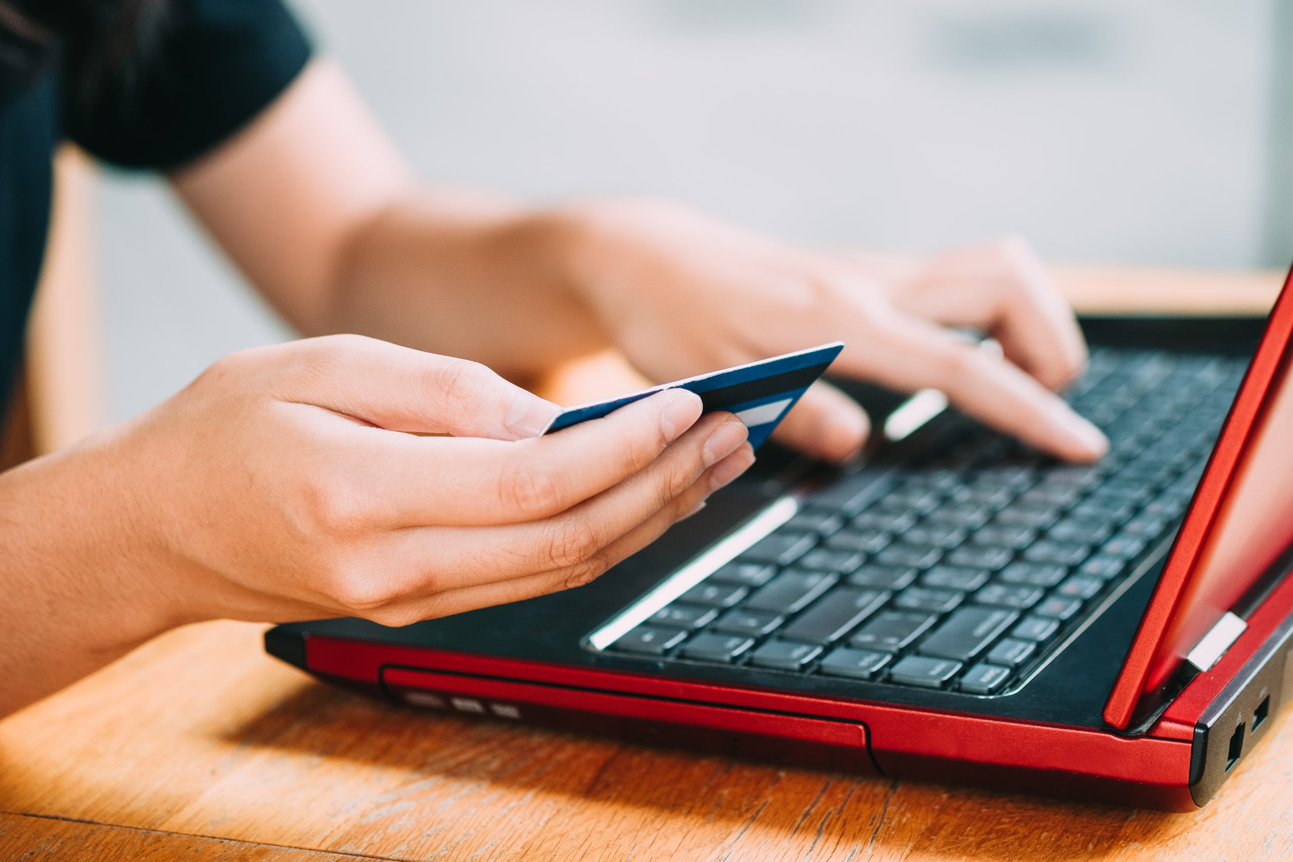 A person holding a bank card while typing on a red laptop. 