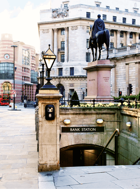 A shot at the of the top of the stairs that lead down to  Bank station tube entrance. In the image we can also see some historic buildings, the back of the equestrian statue of the Iron Duke