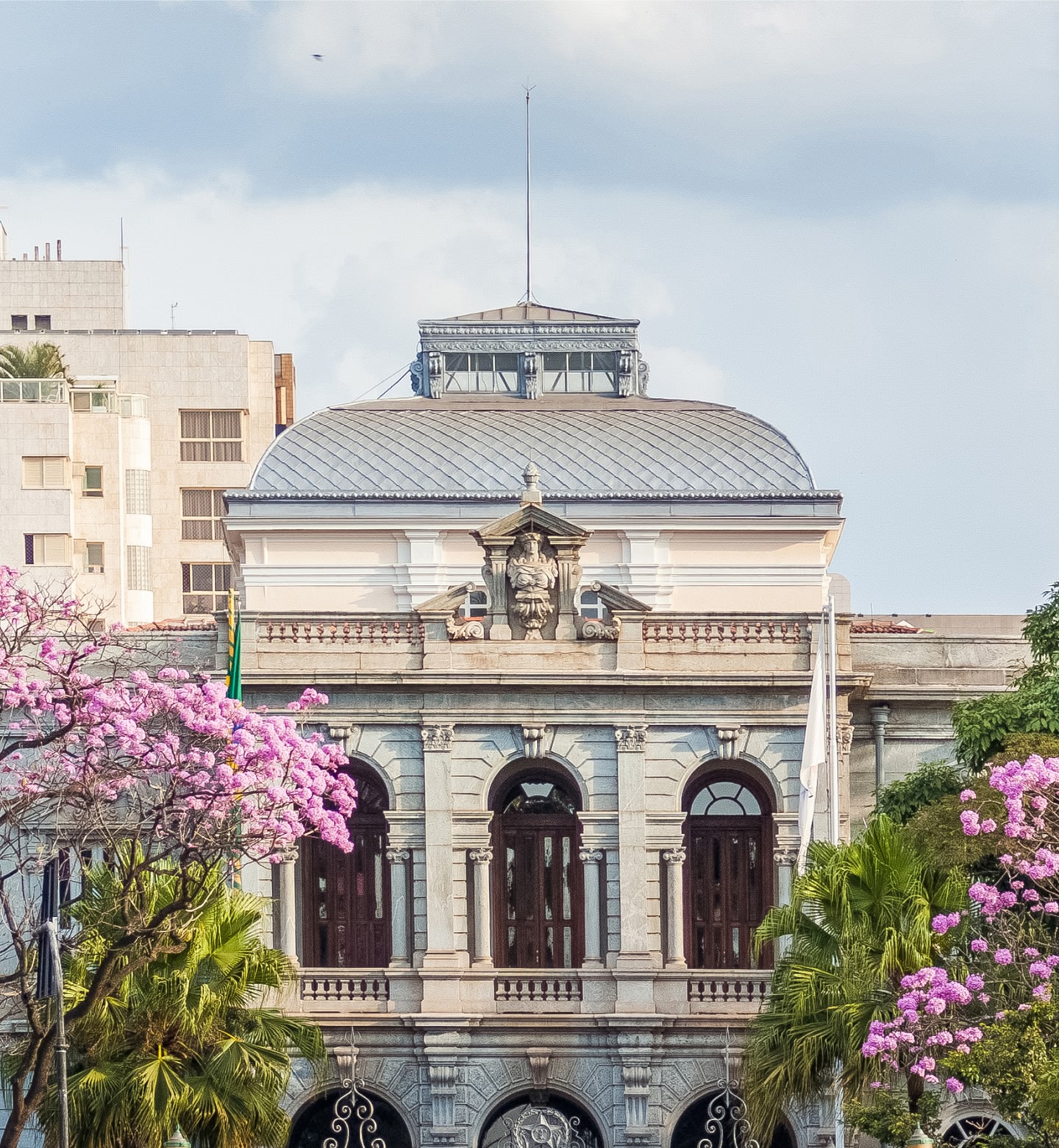 Edifício histórico cinza com janelas em arco e fachada com escultura de leão em Belo Horizonte.
