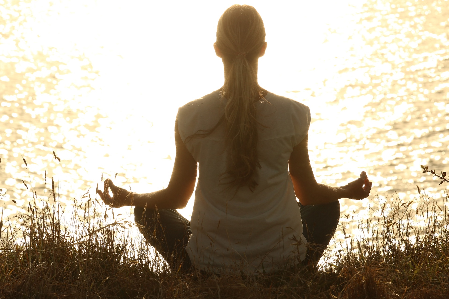 Woman meditates at sunset in front of a body of water.