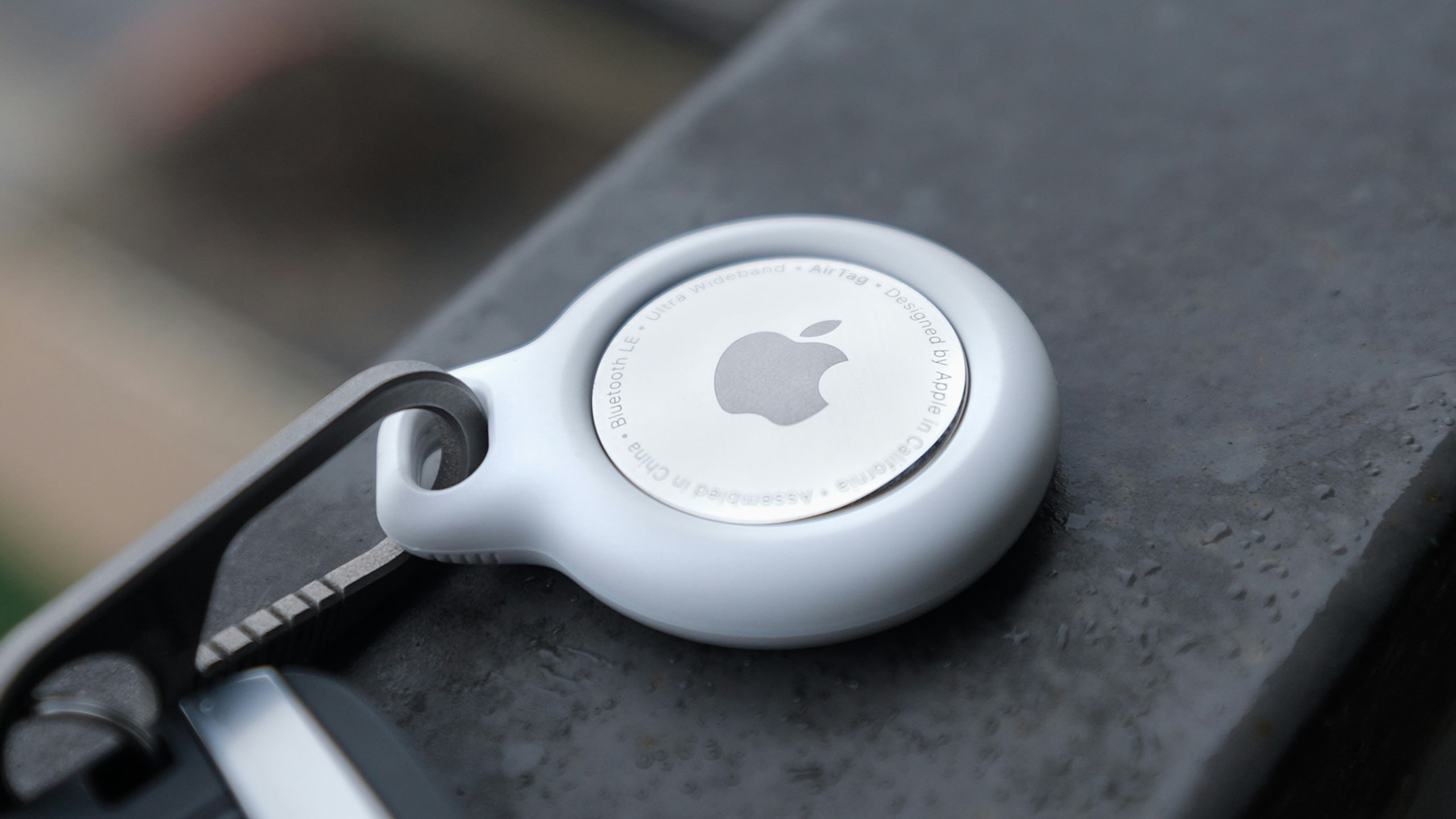 A silver Apple AirTag attached to the zip of a bag.