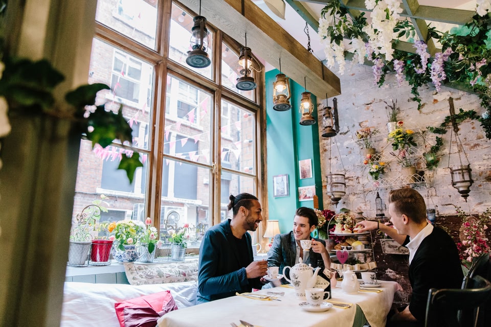 Love is GREAT. Gay men having afternoon tea, Richmond Tearooms, Manchester. Conservatory lined with flowers and lamps. Pots of tea on the table.