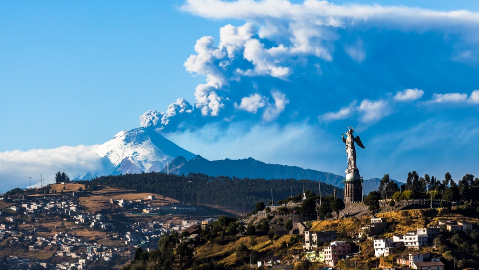Statua della Vergine Maria che domina Quito, con un vulcano fumante in lontananza.
