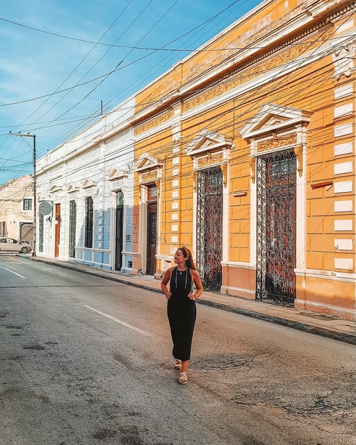 traveller standing in the middle of the road in Merida next to a pastel yellow building during the day.