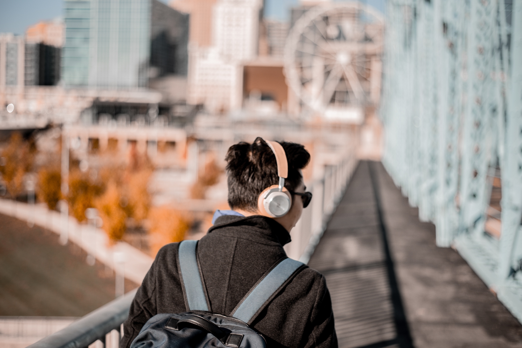 person from behind wearing headphones and a backpack walking along a bridge, cool day.