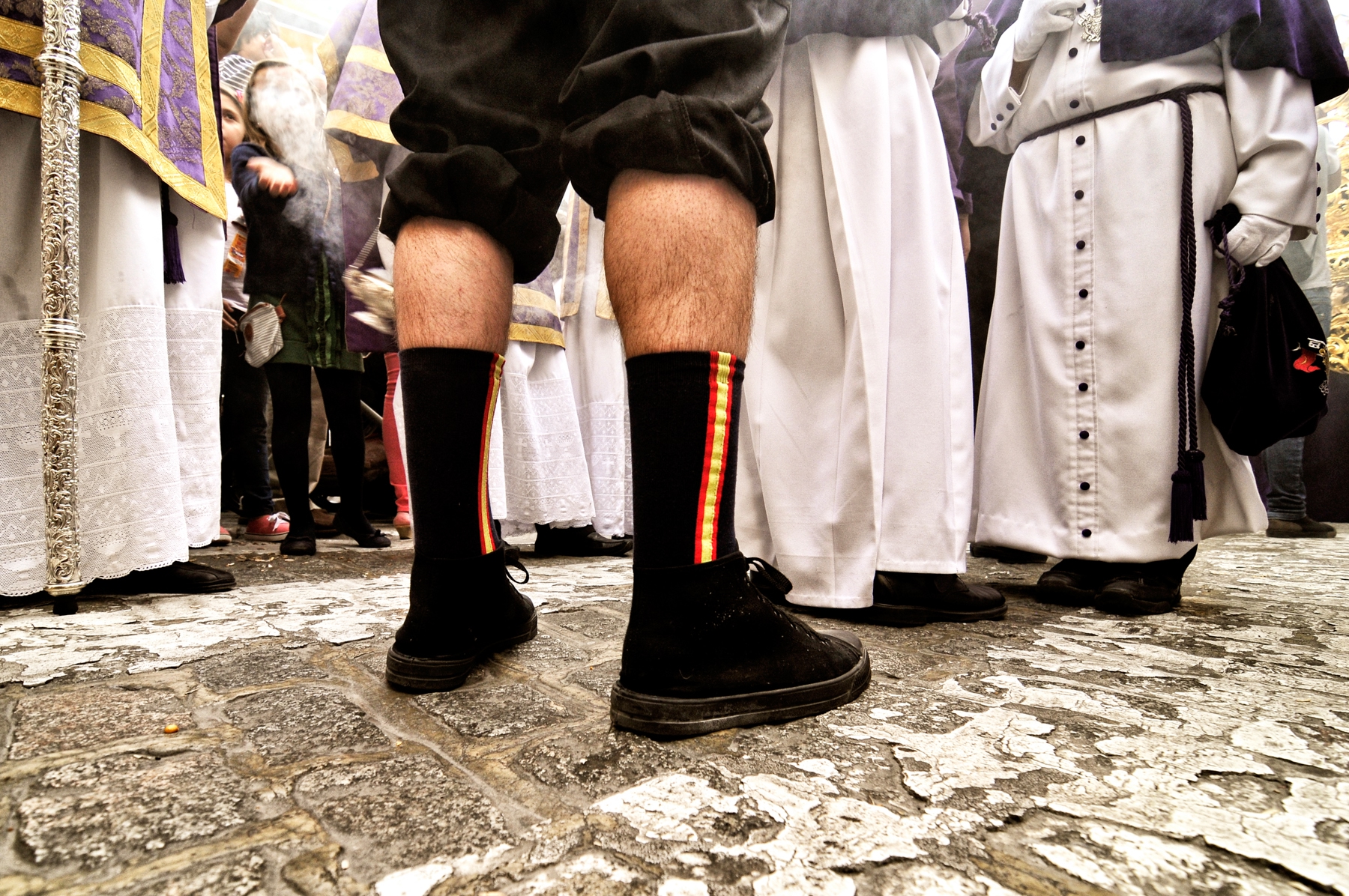Un costalero conversa con varios penitentes y monaguillos durante una procesión © Bisual Studio