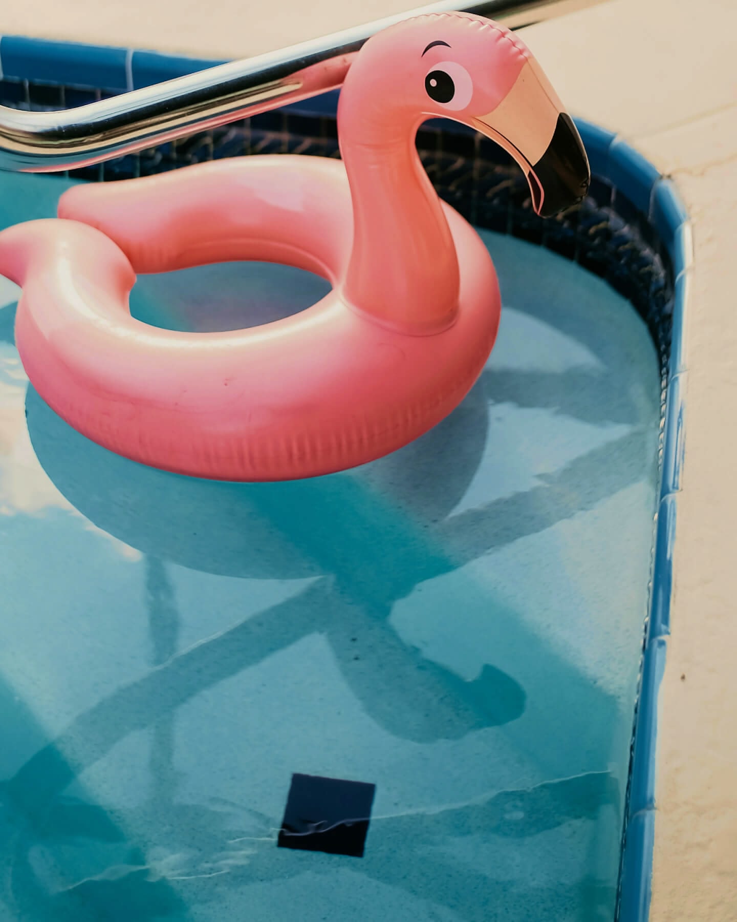Close up of a pink flamingo-shaped inflatable floating in the corner of a pool