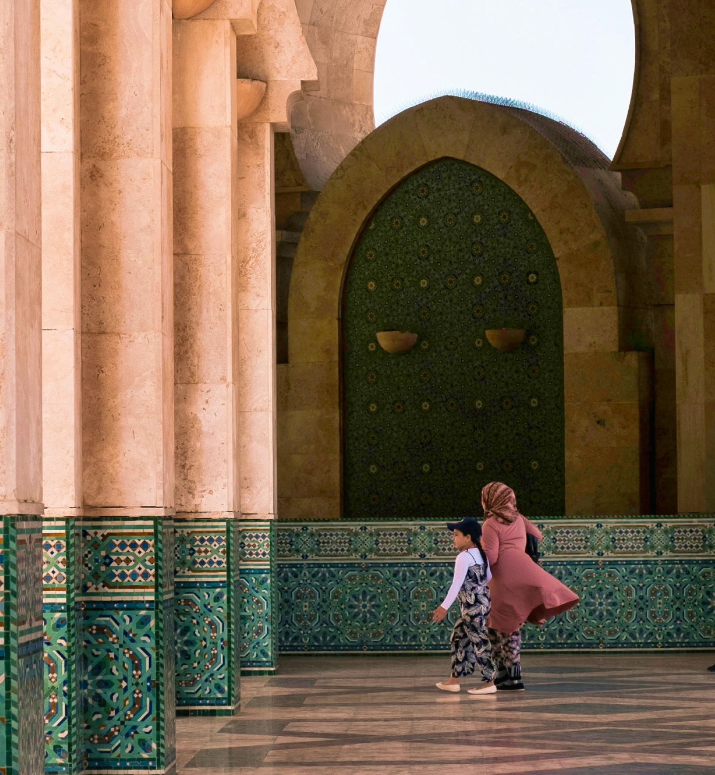 Uma mulher e uma criança andando em um corredor ornamentado com azulejos verdes estampados em Casablanca, Marrocos.