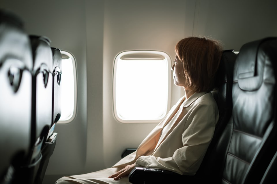 Woman seated on a leather airplane seat looking out the window to her right.