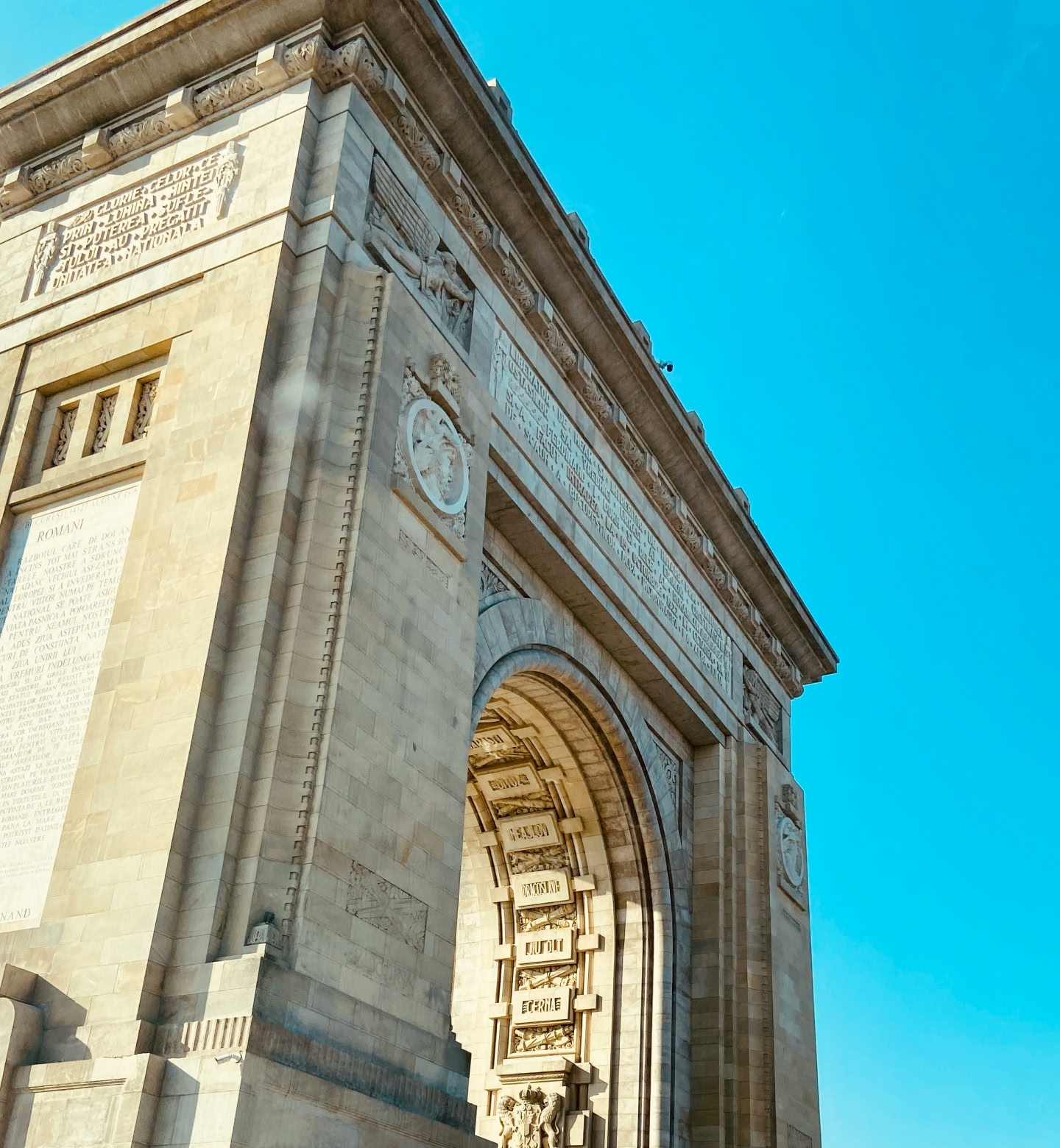 The Triumphal Arch of Bucharest, Romania glowing under a clear blue sky.