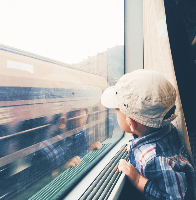 A small child looking out the window of a train at a freight train passing at high speed.
