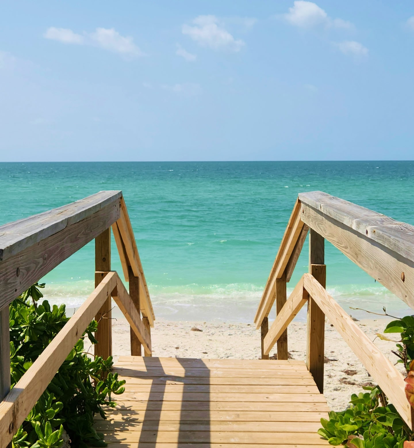 Wooden walkway leading to a turquoise sea and soft sandy beach on Nassau, Bahamas.