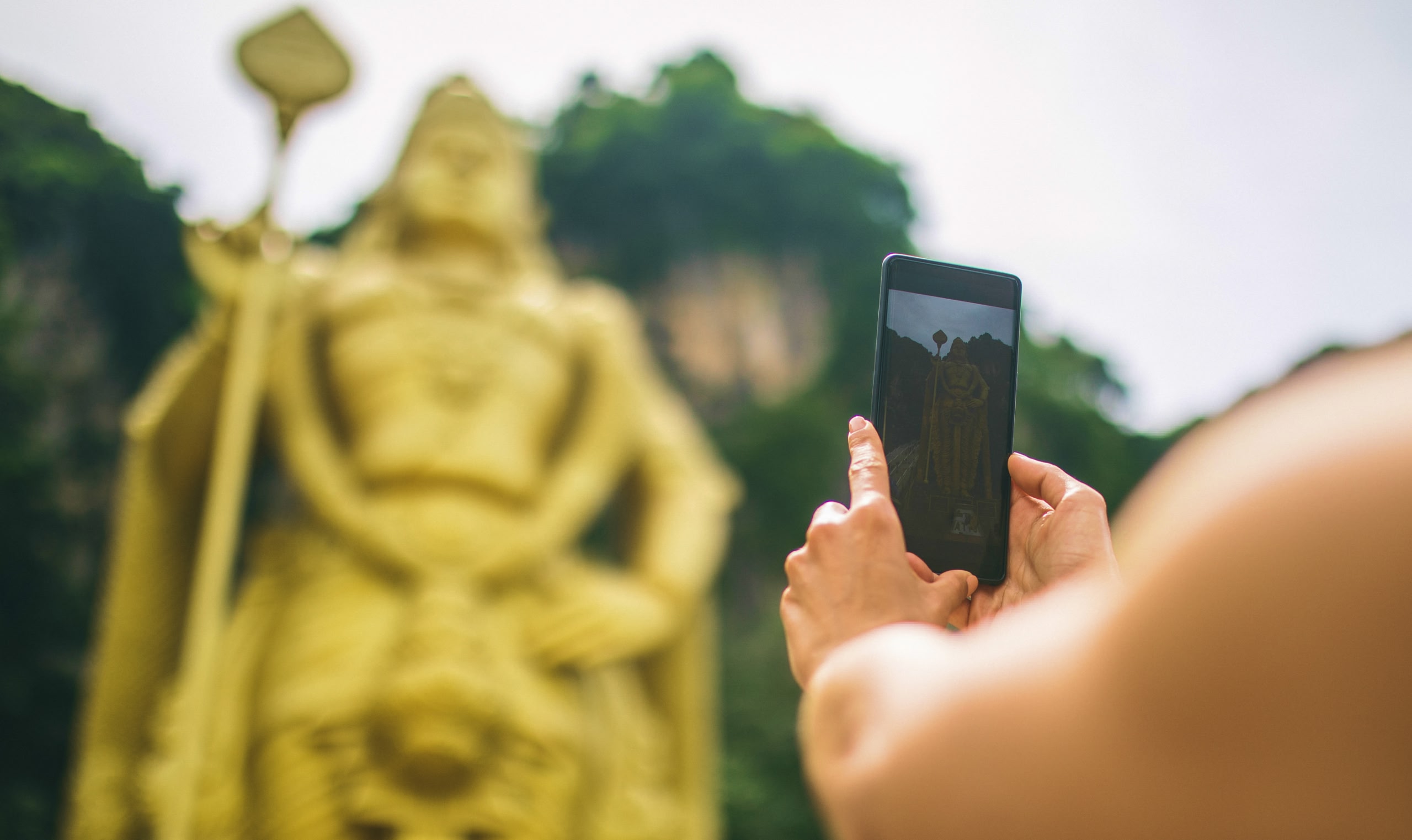 A person takes a picture of a golden statue on their smartphone.