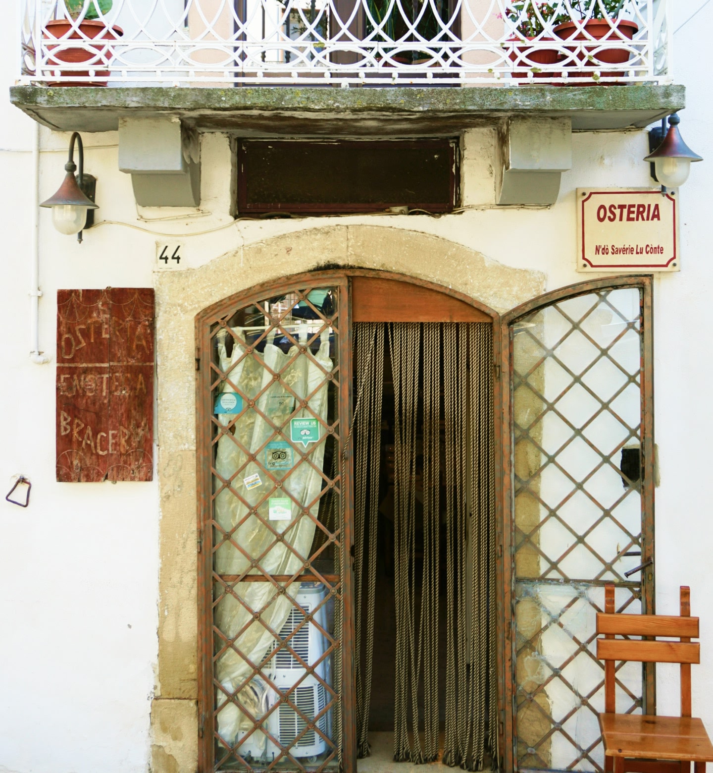 Ein Eingang zu einer rustikalen Osteria mit Eisentoren und einem Holzstuhl davor in Foggia, Italien.