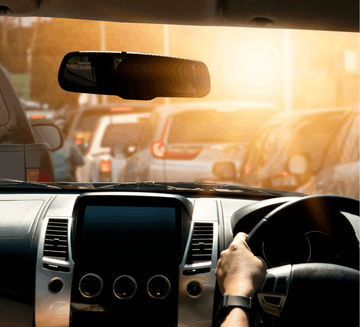Driver's point of view from inside a car, with hands on the steering wheel and sunlight streaming through the windshield