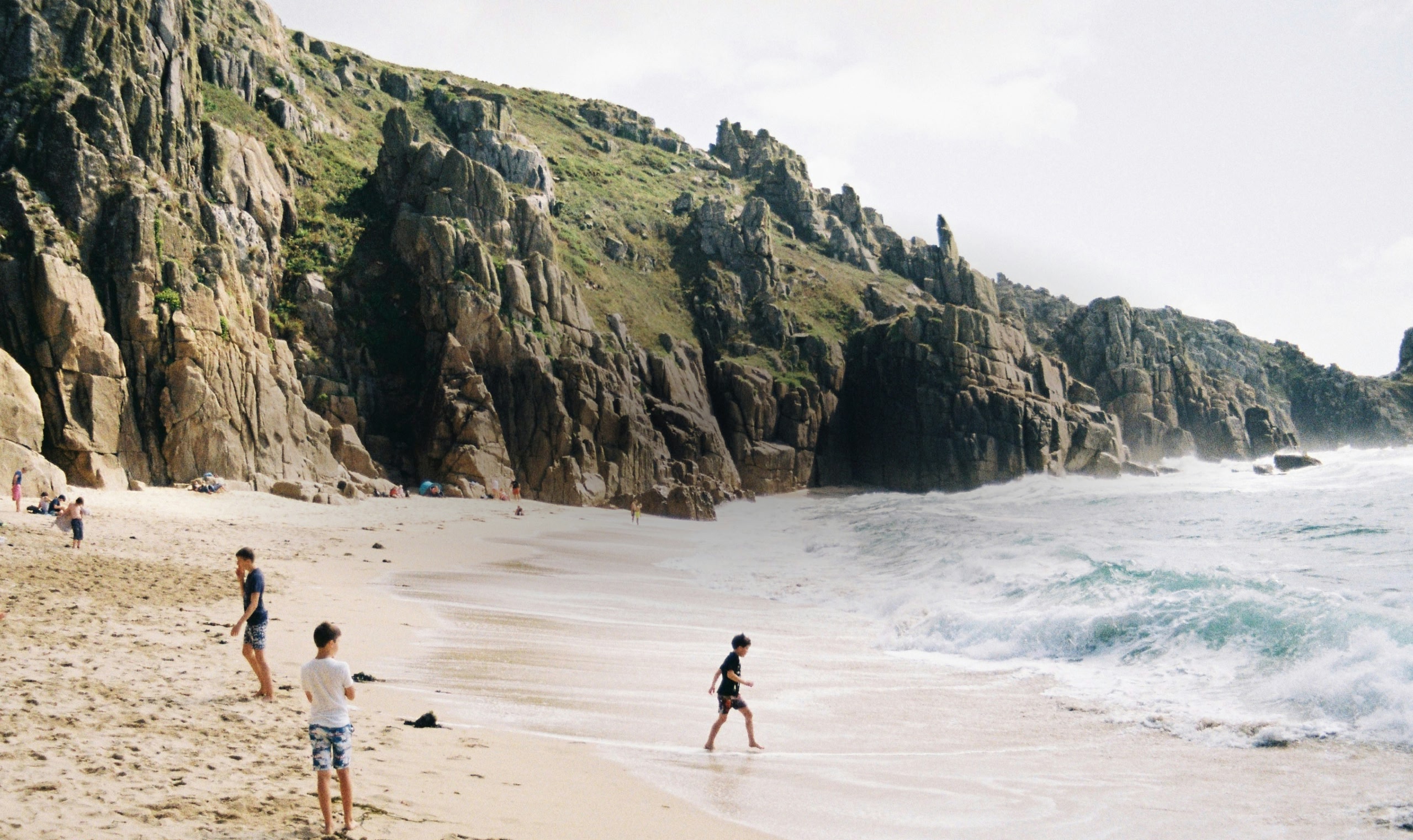 岩の崖を背景にビーチで遊ぶ子どもたち。