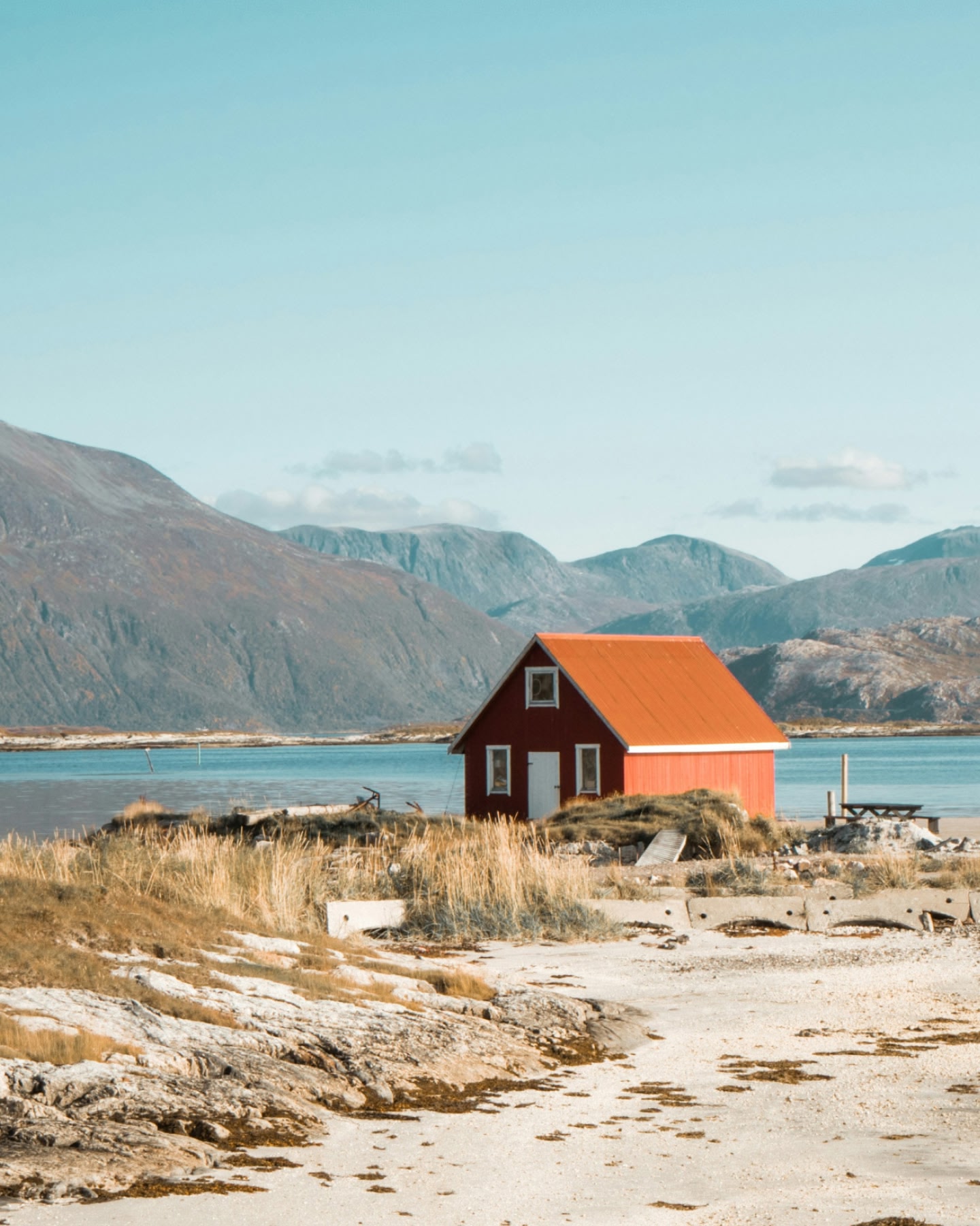 Une cabane rouge se dressant près d'un fjord paisible près de Tromsø, en Norvège, avec des montagnes en arrière-plan.