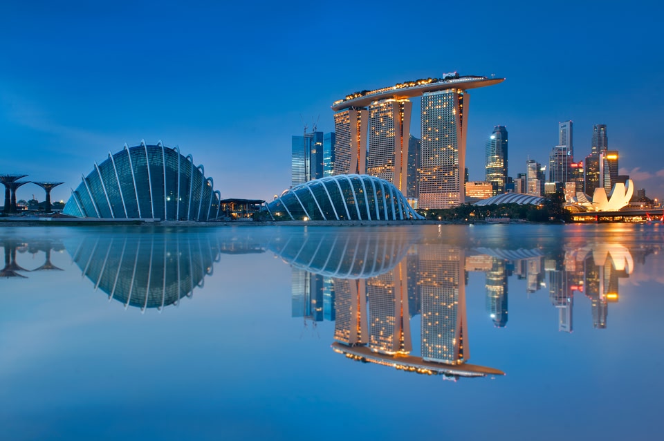 Gardens by the Bay and Singapore skyline reflection on blue water at blue hour in Singapore.
