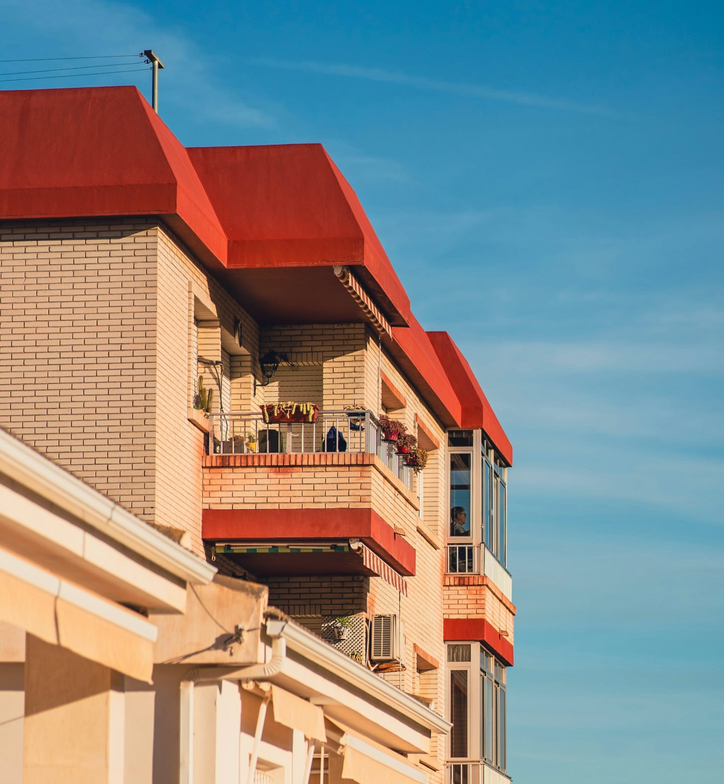 Pale orange brick apartment building with a bright red roof against a blue sky in Murcia, Spain