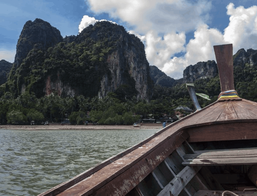A captivating point-of-view shot capturing the front of a long boat gracefully navigating the pristine waters of Railay Beach, surrounded by stunning coastal scenery.