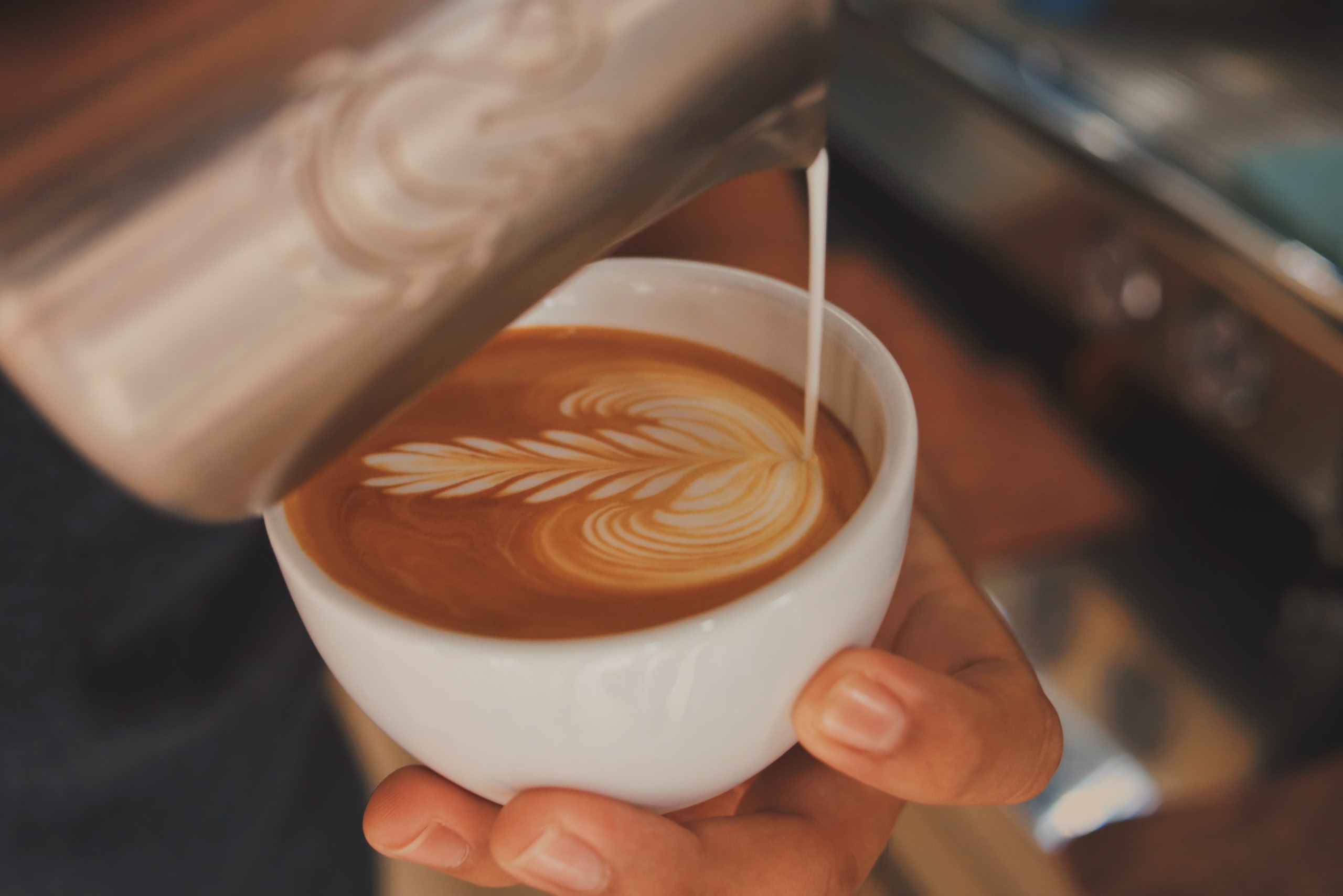 Milk being poured into a coffee making flower latte art. 
