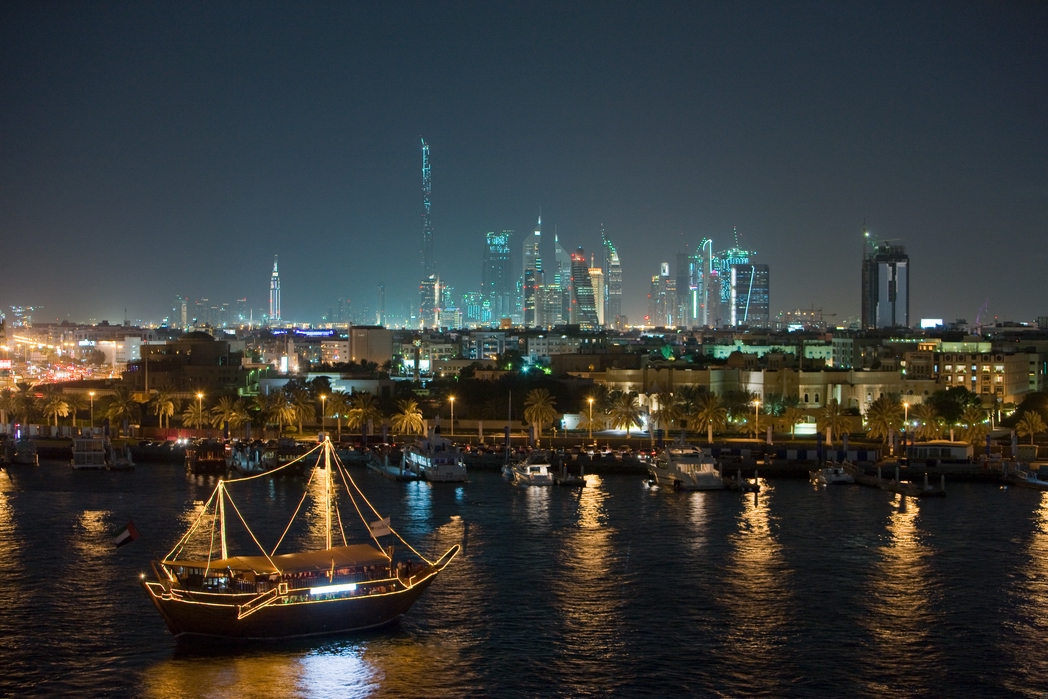 illuminated tourist dhow on Dubai Creek with the skyscrapers of Sheikh Zayed Road in the background including the Burj Dubai - the worlds tallest building