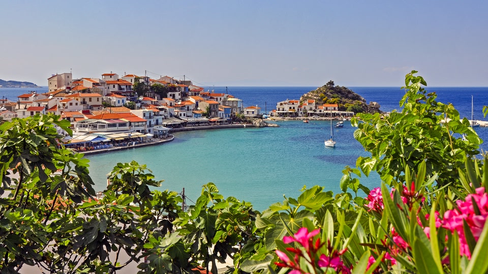 A scenic coastal view of a village in Samos, Greece, with clear blue waters and vibrant greenery.