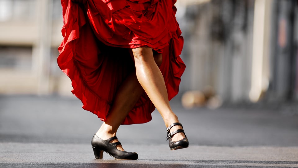 A person wearing a vibrant red dress and black shoes, walking on a street.