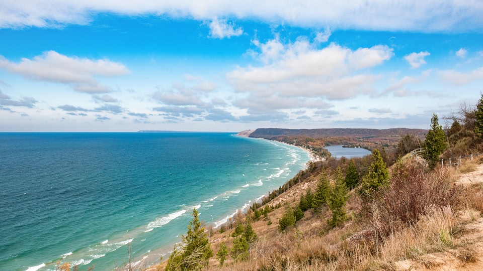 A scenic view of the ocean and shoreline from a hill with clear blue skies.