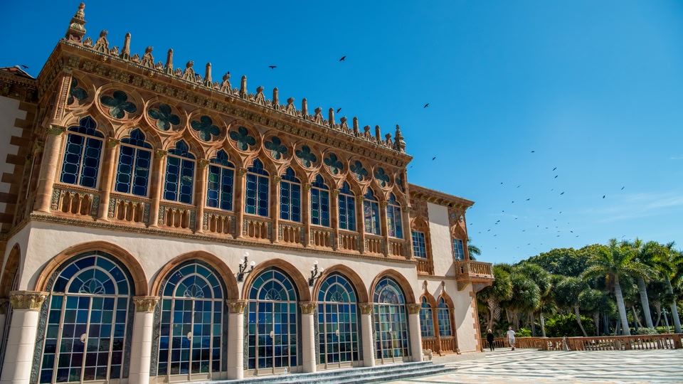 An ornate building with many arched windows and intricate design, under a clear blue sky with birds flying overhead.