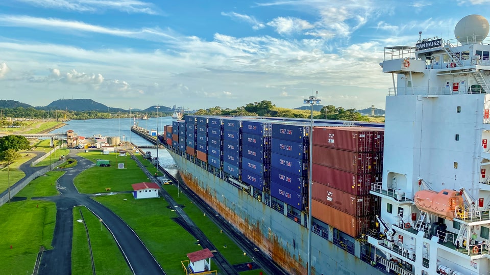 Container ship in a Panama City lock with stacked blue and red shipping containers.
