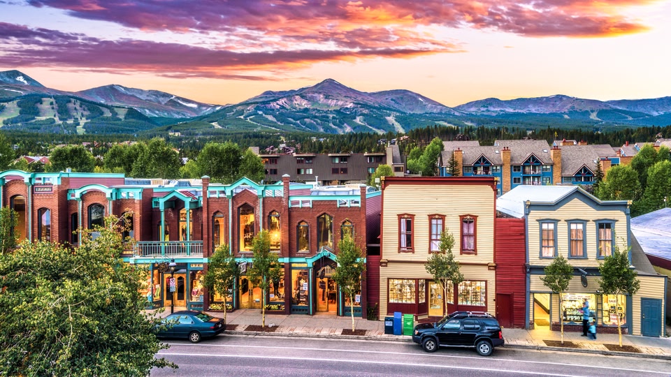 A scenic view of a small town with colorful buildings and a mountain range in the background during sunset