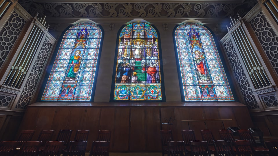 Interior of a church with three large stained glass windows depicting religious scenes.