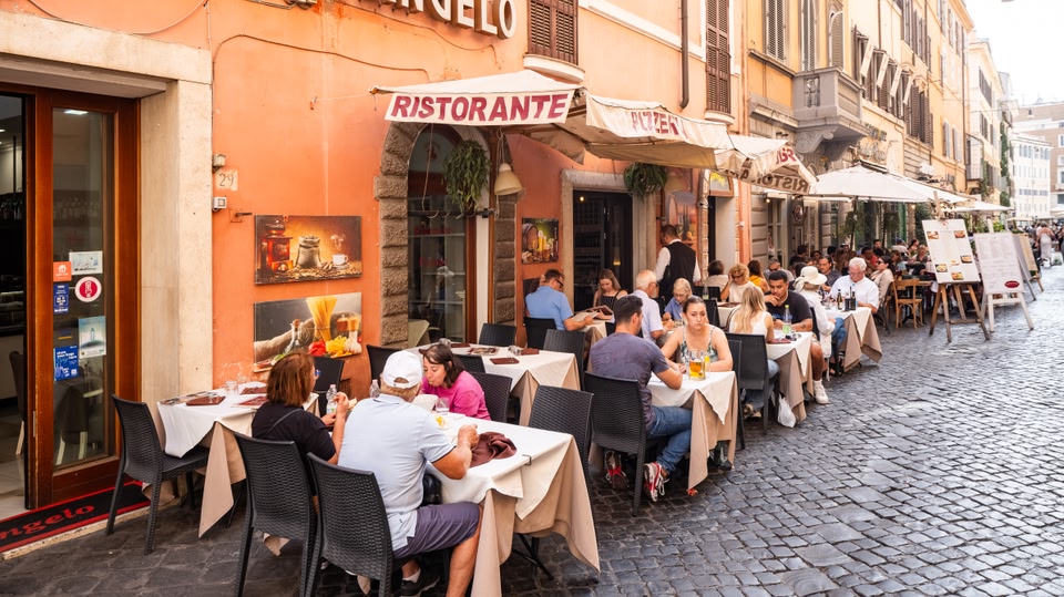 Outdoor dining area with people seated at tables under umbrellas on a cobblestone street.