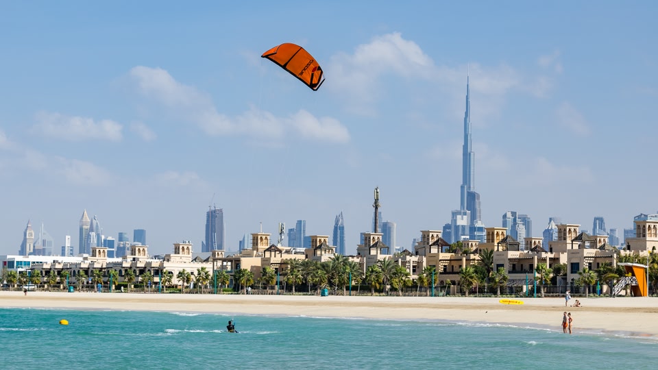 A person kitesurfing in the ocean near a beach with a cityscape in the background.