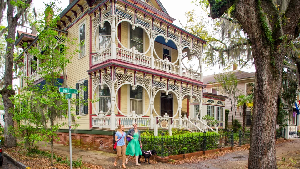 Two women walking on a sidewalk in front of an ornate historic house in Savannah, Georgia.