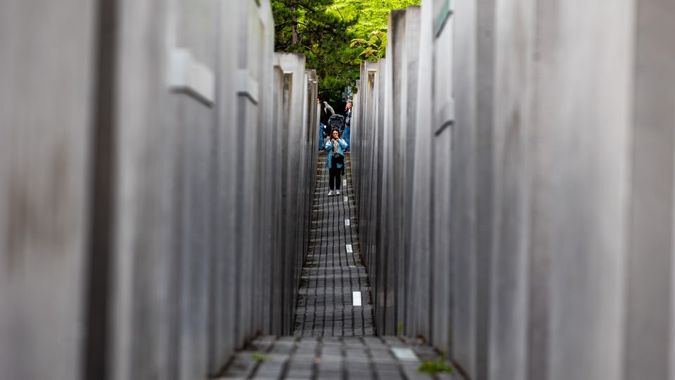 A narrow concrete pathway between tall, rectangular concrete blocks, part of the Memorial to the Murdered Jews of Europe in Berlin.