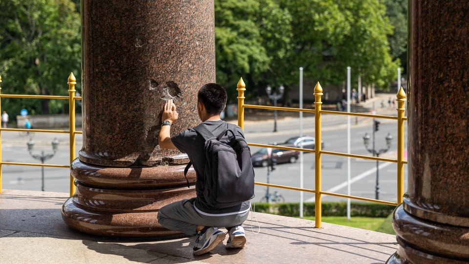 A man kneeling and touching a historical monument with a busy street in the background.
